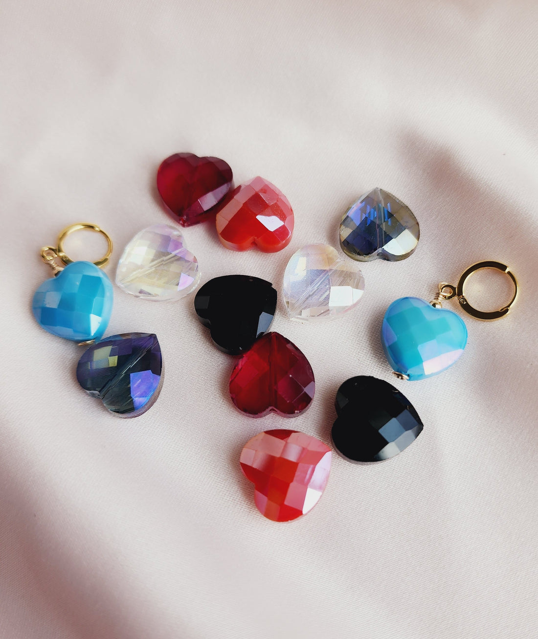 Top View A collection of Ella Huggie Heart Earrings in various colors including blue, red, purple, and clear, displayed on a pale background.